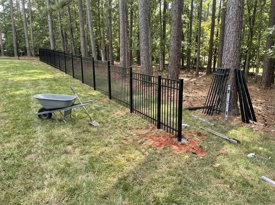 Black aluminum fence panels following the grade of a sloping side yard under pines