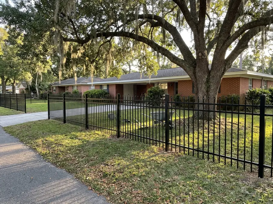 A black aluminum fence with staggered spear tops in front of a brick ranch house