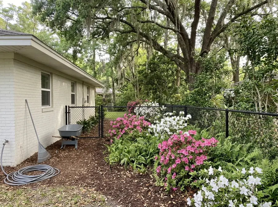 Black vinyl-coated chain link fence along a planted bed beside a brick ranch house