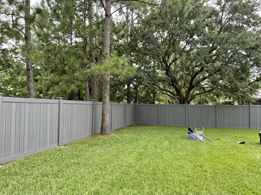 A gray composite privacy fence with tight vertical boards and flat post caps around a backyard
