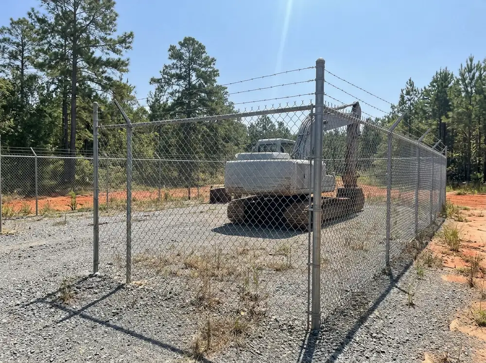 Eight-foot galvanized chain link fence topped with angled barbed wire arms around an equipment yard