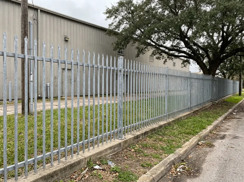 Galvanized steel palisade fence with pointed pales around an industrial building