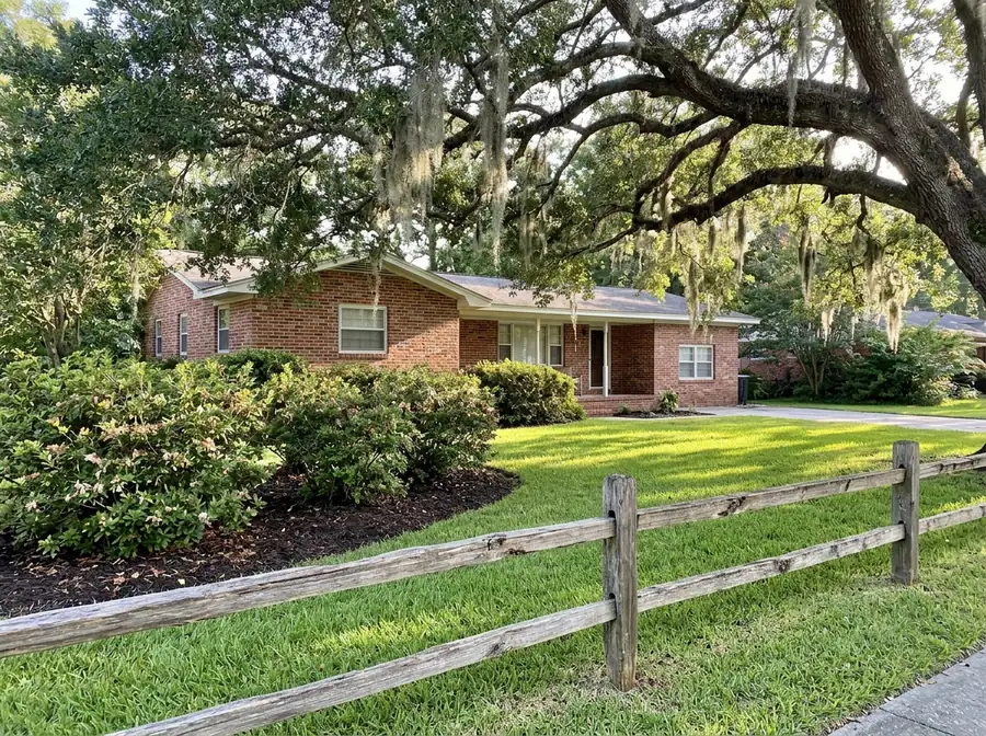 A two-rail wood split rail fence edging a front lawn and flower bed beside a brick ranch house