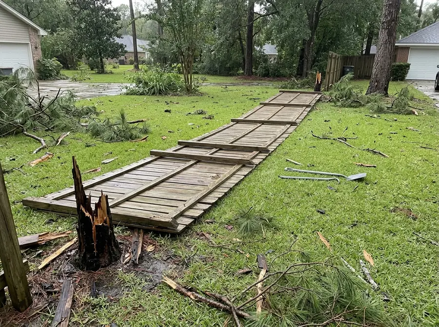 A privacy fence section blown flat on the lawn with posts snapped off at ground level