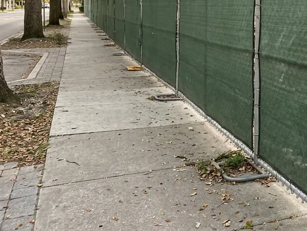 Temporary fence panels wrapped in dark green privacy screen along a construction site