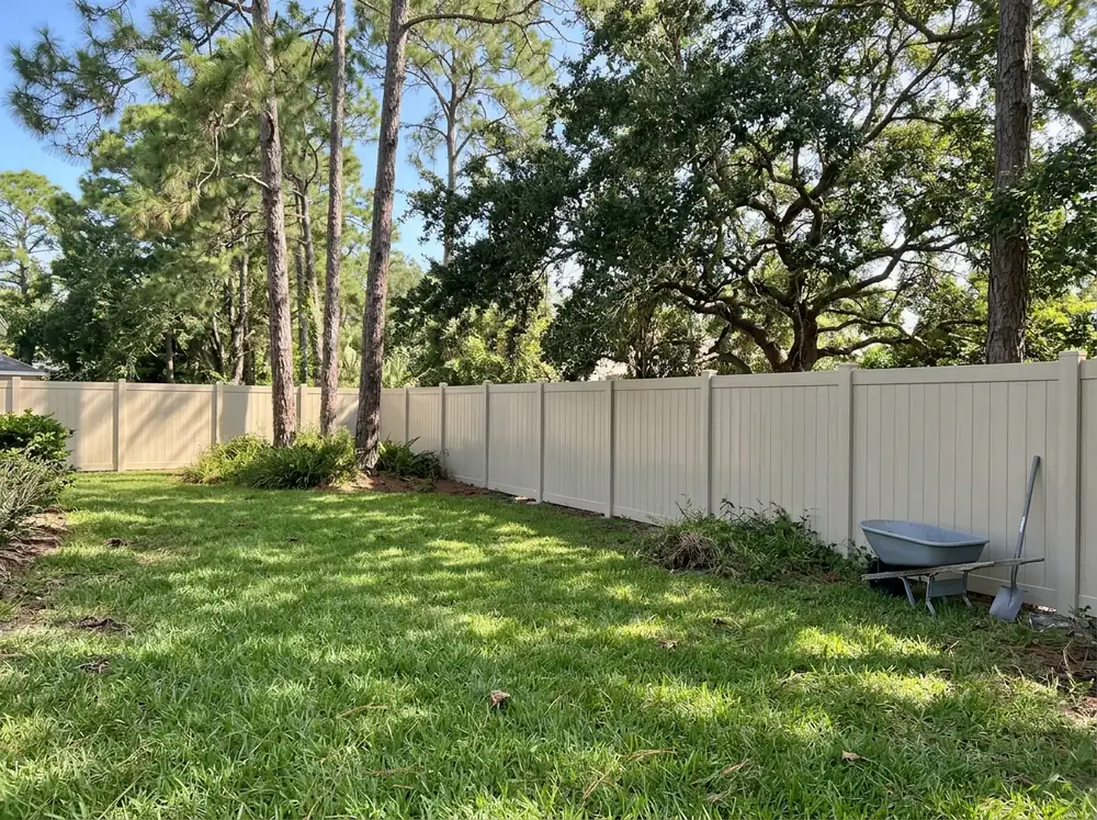 A tan solid vinyl privacy fence with flat post caps along a backyard lawn